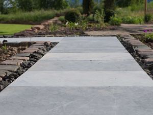Hardstenen platen als tuinpad, met bloembedden en een groen gazon op de achtergrond