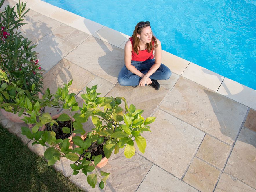 Zandstenen terras met zuidelijke flair Vrouw zittend op zandstenen terras bij het zwembad van bovenaf gefotografeerd