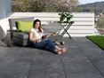 Jonge vrouw leest op terras met donkere porcellanato tegels met leisteenlook en modern meubilair