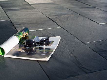 Een tijdschrift en een zonnebril op leien in de zon