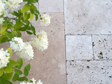 Beige travertin tegels gelegd in een gemengd patroon met witte bloemen van bovenaf