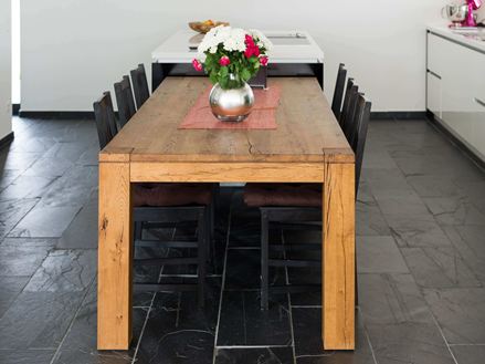 Houten eettafel in combinatie met donkere leistenen vloer en witte muren