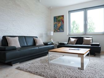 Woonkamer met natuurstenen lambrisering aan de muur en een zwarte bank
